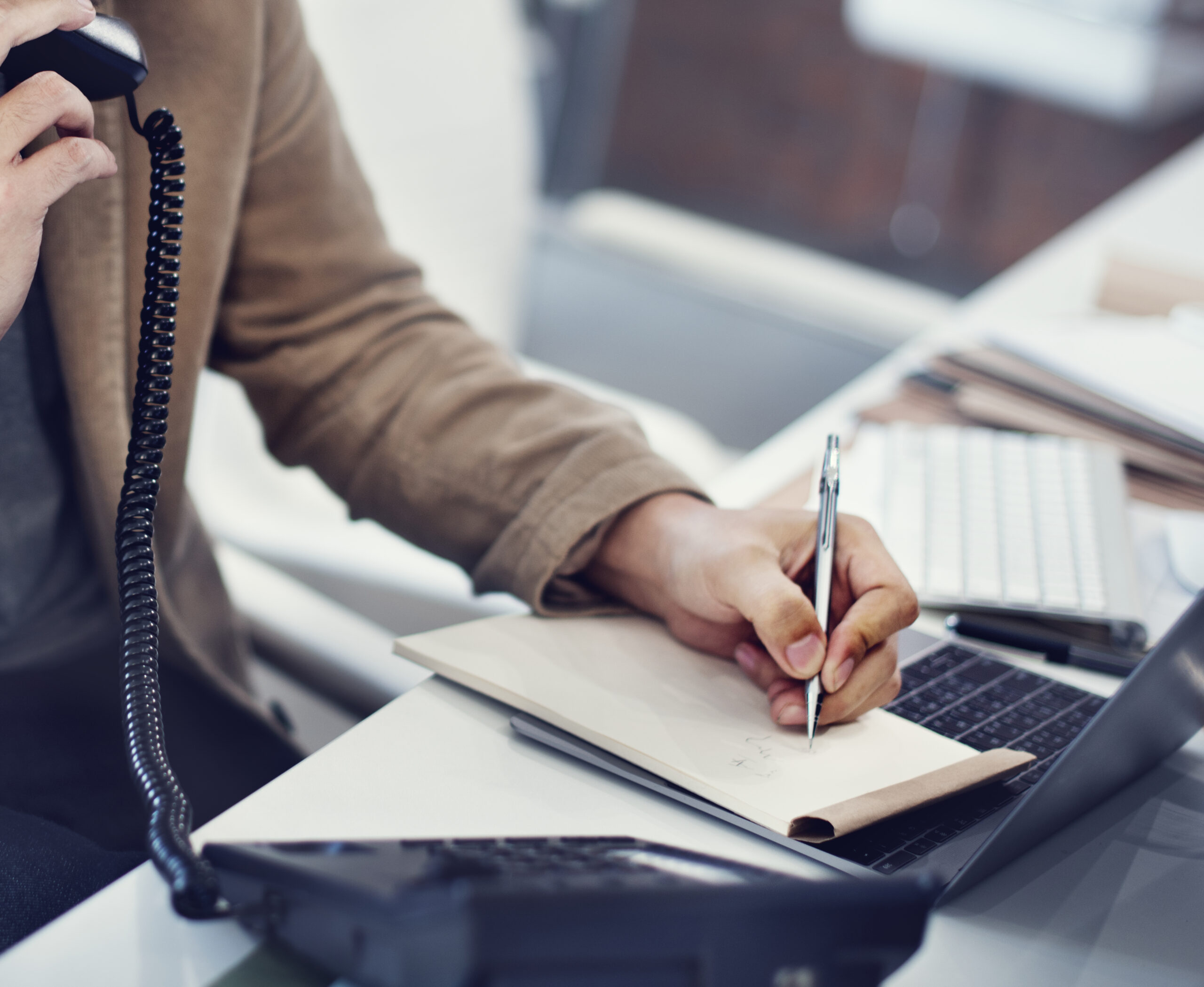 closeup of hand writing note while on the phone